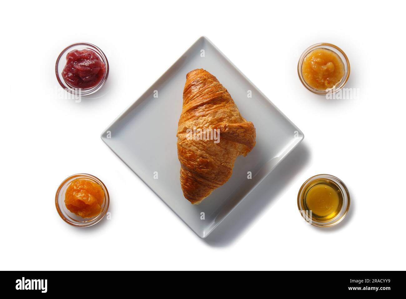 Croissant auf einer quadratischen Untertasse und verschiedene Arten von Marmelade und Honig in Schüsseln. Isoliert auf weißem Hintergrund. Stockfoto