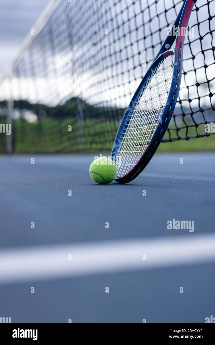 Nahaufnahme von Tennisball und Tennisschläger gegen Netz auf Tennisplatz an bewölktem Tag, Kopierbereich Stockfoto