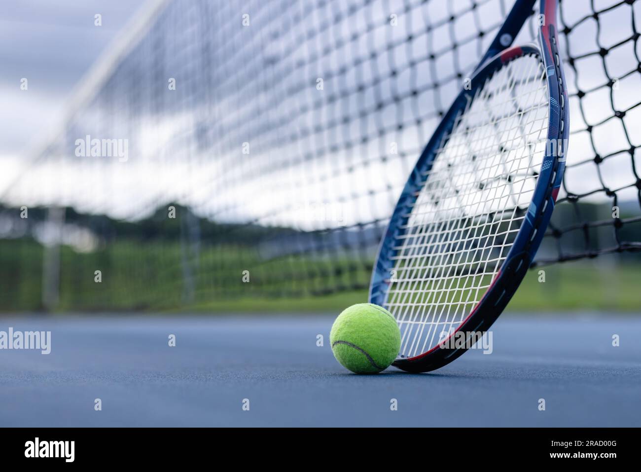 Nahaufnahme von Tennisball und Tennisschläger gegen Netz auf Tennisplatz an bewölktem Tag, Kopierbereich Stockfoto