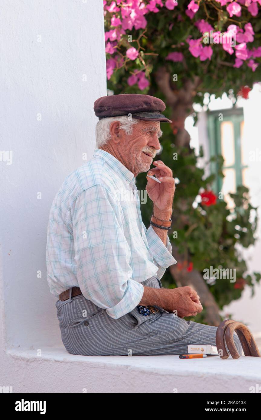 Nahaufnahme eines alten Griechen, der eine Zigarette raucht, während er auf einer niedrigen Mauer in Santorin, Griechenland sitzt Stockfoto
