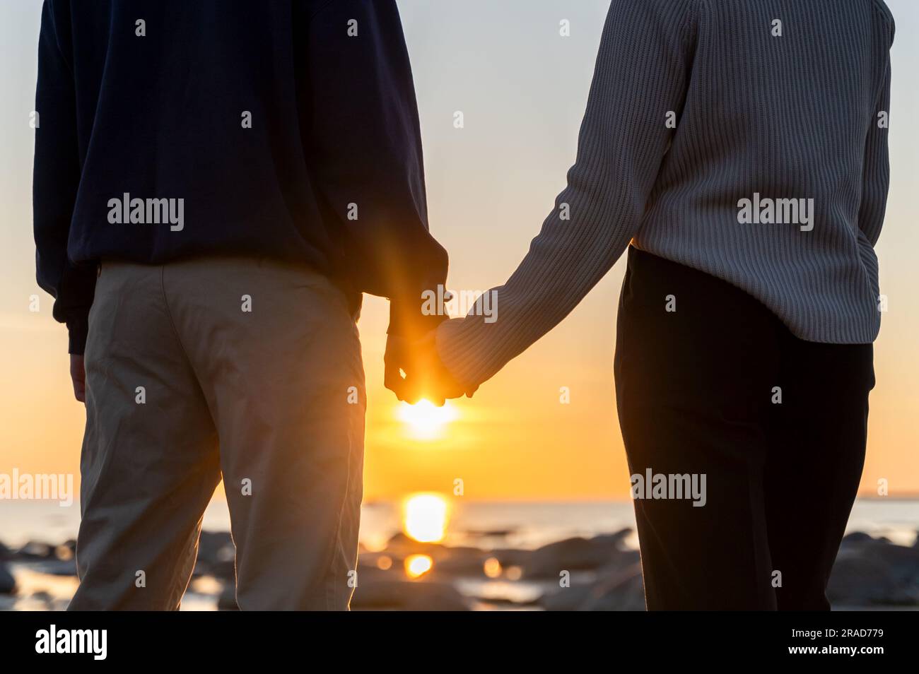 Zwei Personen, die bei Sonnenuntergang die Hand gegen den blauen Himmel halten. Blick von hinten direkt auf die Sonne Stockfoto