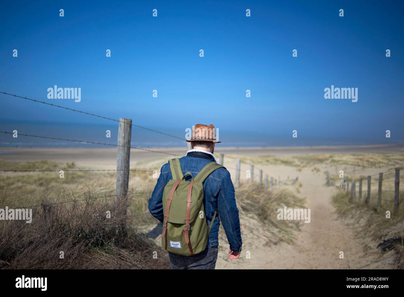 Ein Mann mit blauen Jeans und Strohhut genießt einen Spaziergang in den Dünen Stockfoto