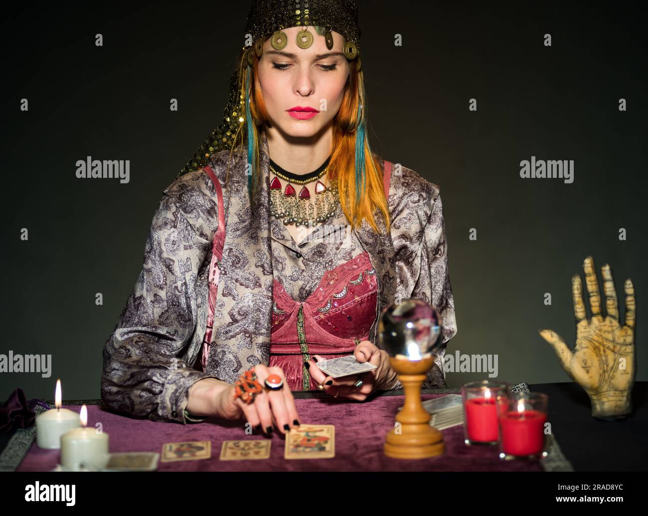 Erwachsenenfokussierte weibliche Wahrsagerin, die Tarotkarten liest, am Tisch mit Kerzen und magischer Kristallkugel Konzept der Enthaltsamkeit, Astrologie und Esote Stockfoto