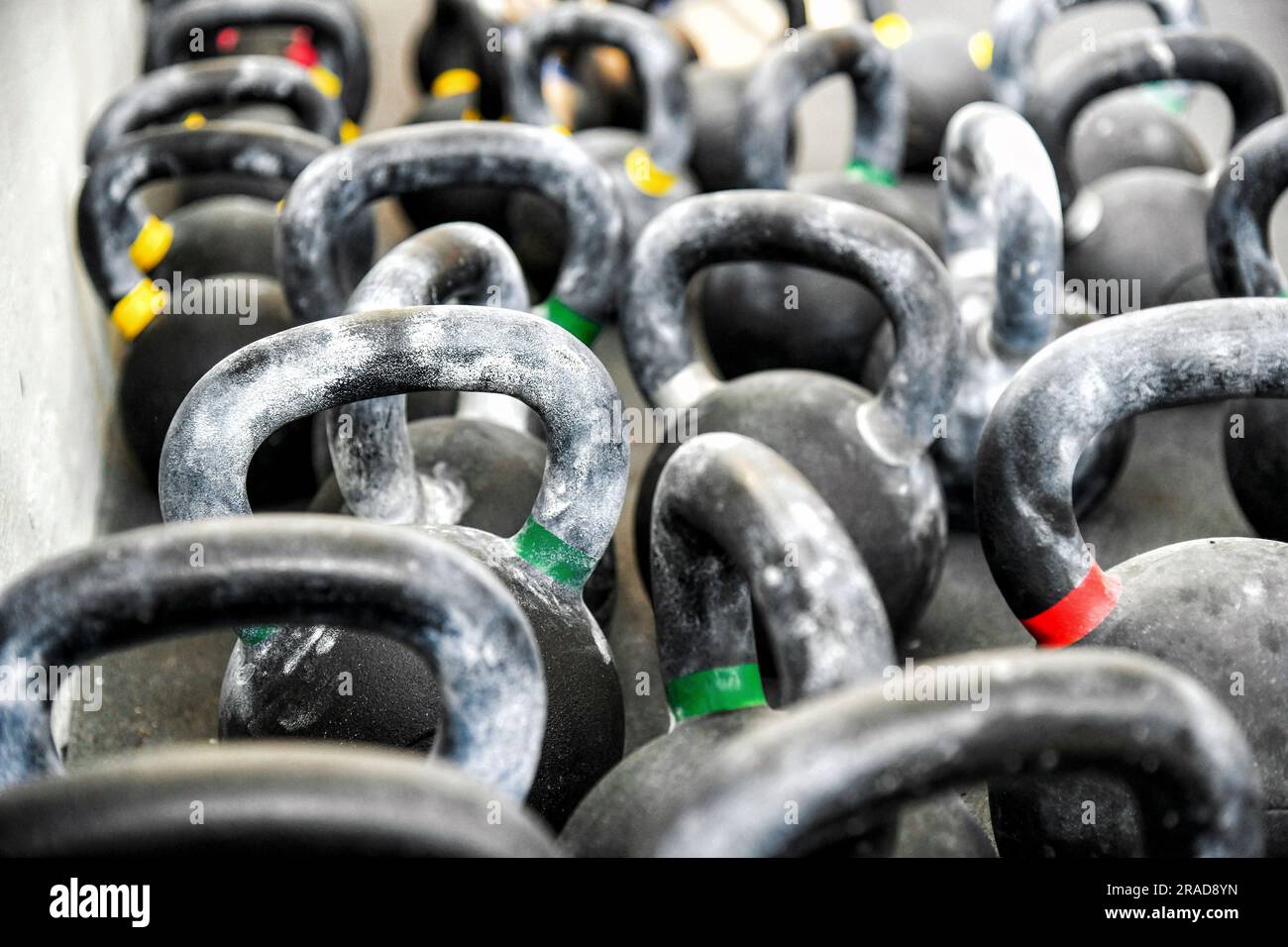 Nahaufnahme einer Reihe von schweren Metallkettlebells mit bunten Streifen und Griffen, die auf dem Boden in einem modernen, leichten Fitnessstudio gestapelt sind Stockfoto