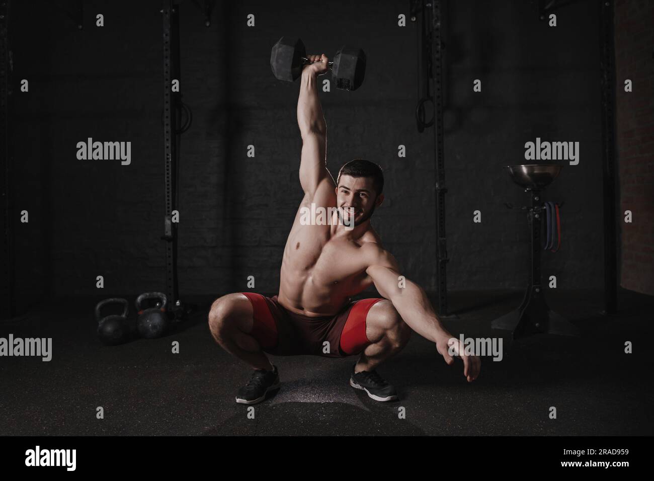 Ein Mann ohne Oberkörper, der Kurzhanteln macht und lächelt. Ein hübscher Crossfit-Athlet, der funktionelles Training macht. Stockfoto