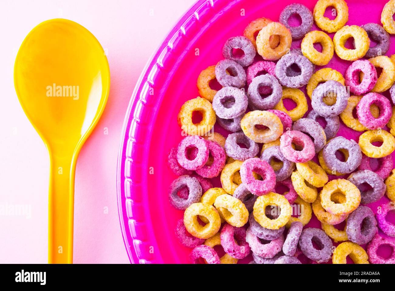 Draufsicht auf einem rosafarbenen Teller mit Cornflakes neben einem orangefarbenen Löffel Stockfoto