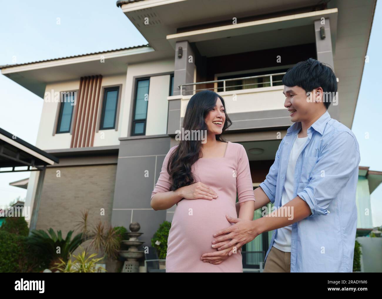 Glückliche Familie steht vor ihrem Haus, Ehemann und schwangere Frau Stockfoto