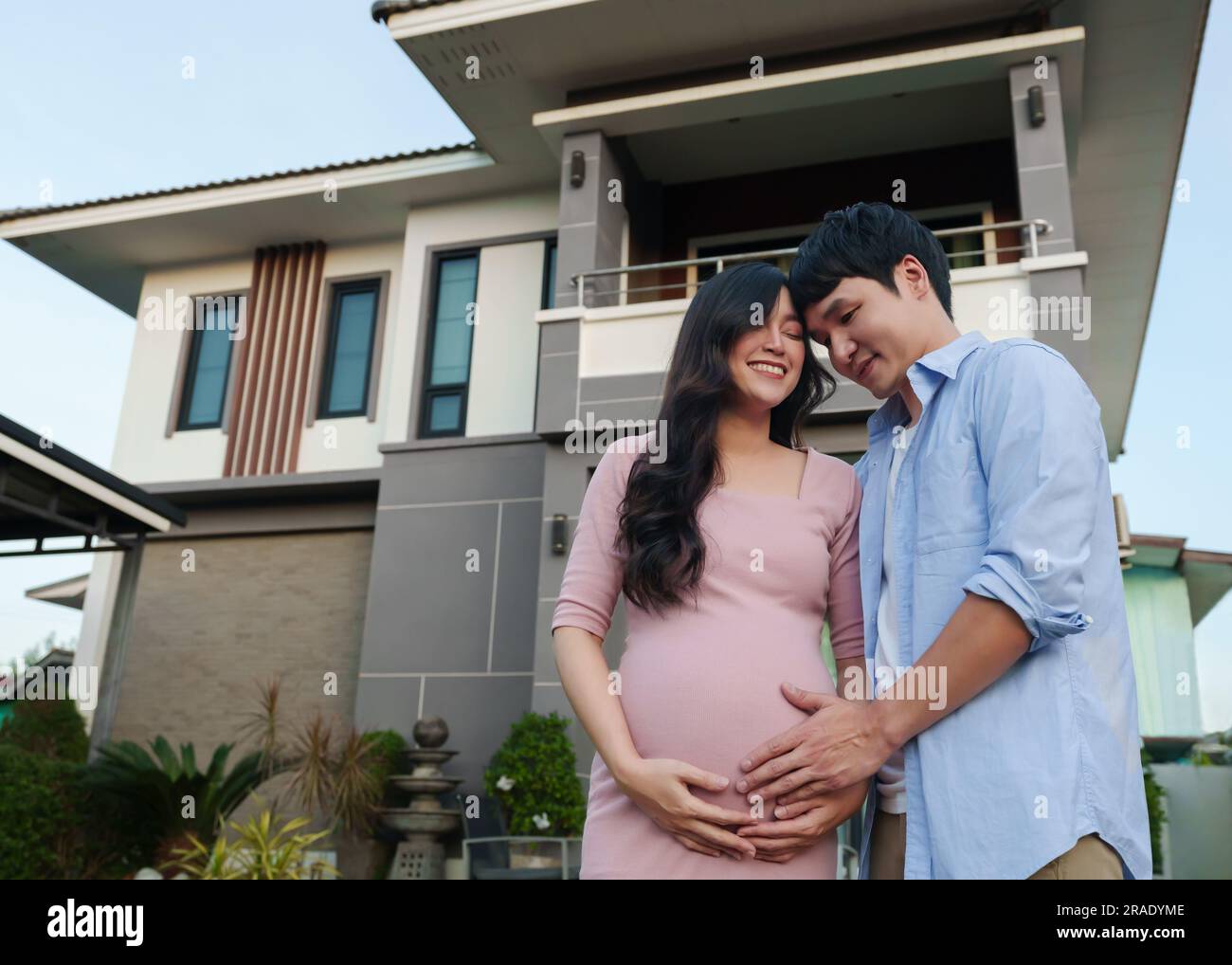 Glückliche Familie steht vor ihrem Haus, Ehemann und schwangere Frau Stockfoto