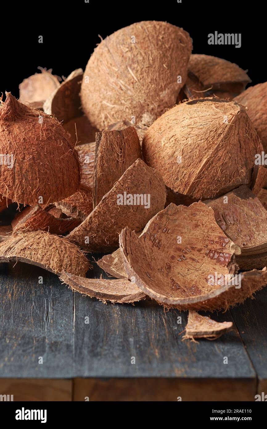 Teile von Kokosnussschalen auf schwarzer Holzoberfläche, kommerziell wichtiges Fasermaterial, das als Brennstoff verwendet wird, Inhaltsstoff in verschiedenen Produkten, s. Stockfoto