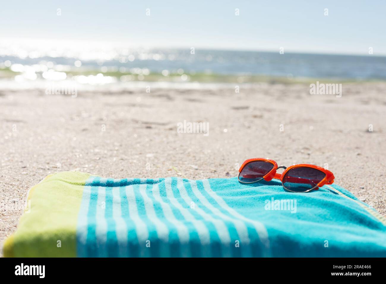 Rote Sonnenbrille auf grün-blau gestreiftem Handtuch am sonnigen Sandstrand am Meer, Kopierbereich Stockfoto