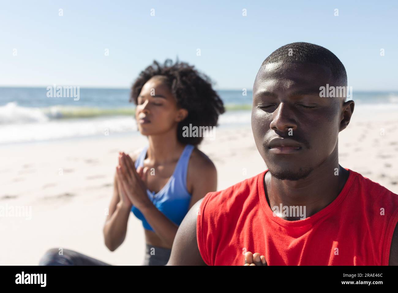 Glückliches, fittes afroamerikanisches Paar, das Yoga-Meditation praktiziert und am sonnigen Strand sitzt Stockfoto