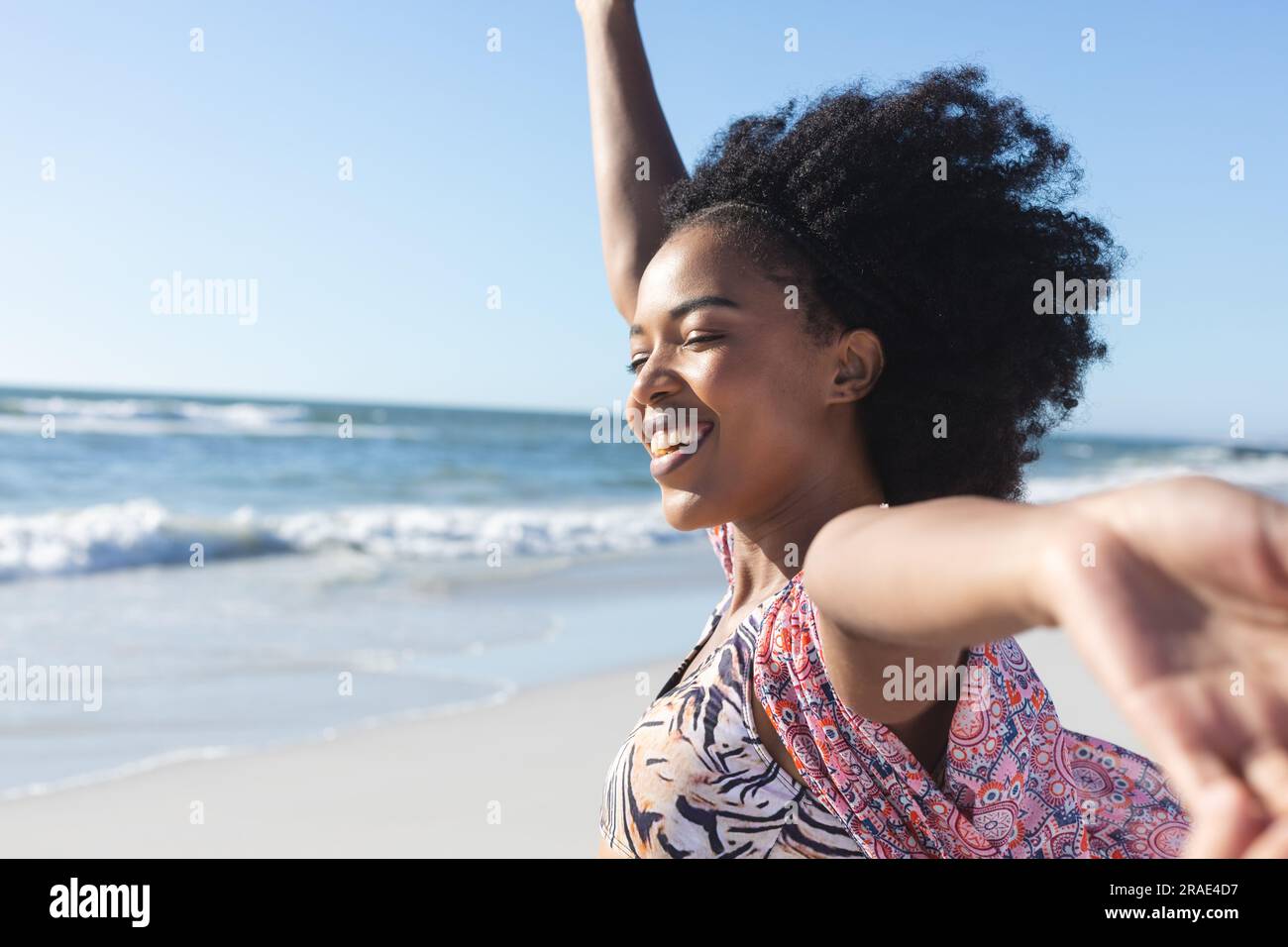 Glückliche afroamerikanische Frau, die mit ausgestreckten Armen am sonnigen Strand am Meer lächelt, Kopierraum Stockfoto