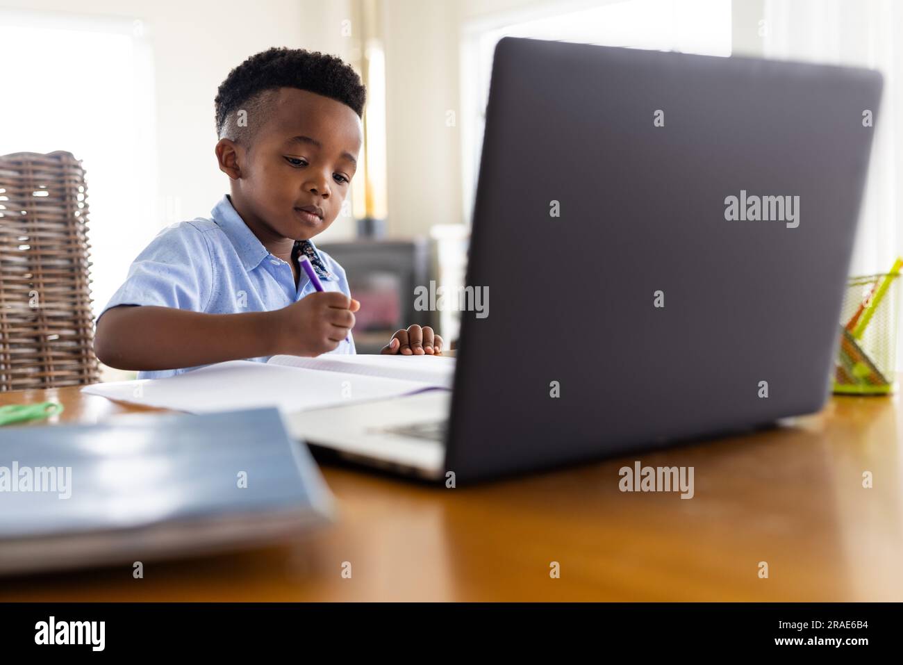 Ein afroamerikanischer Junge sitzt am Tisch und benutzt einen Laptop für den Online-Unterricht Stockfoto