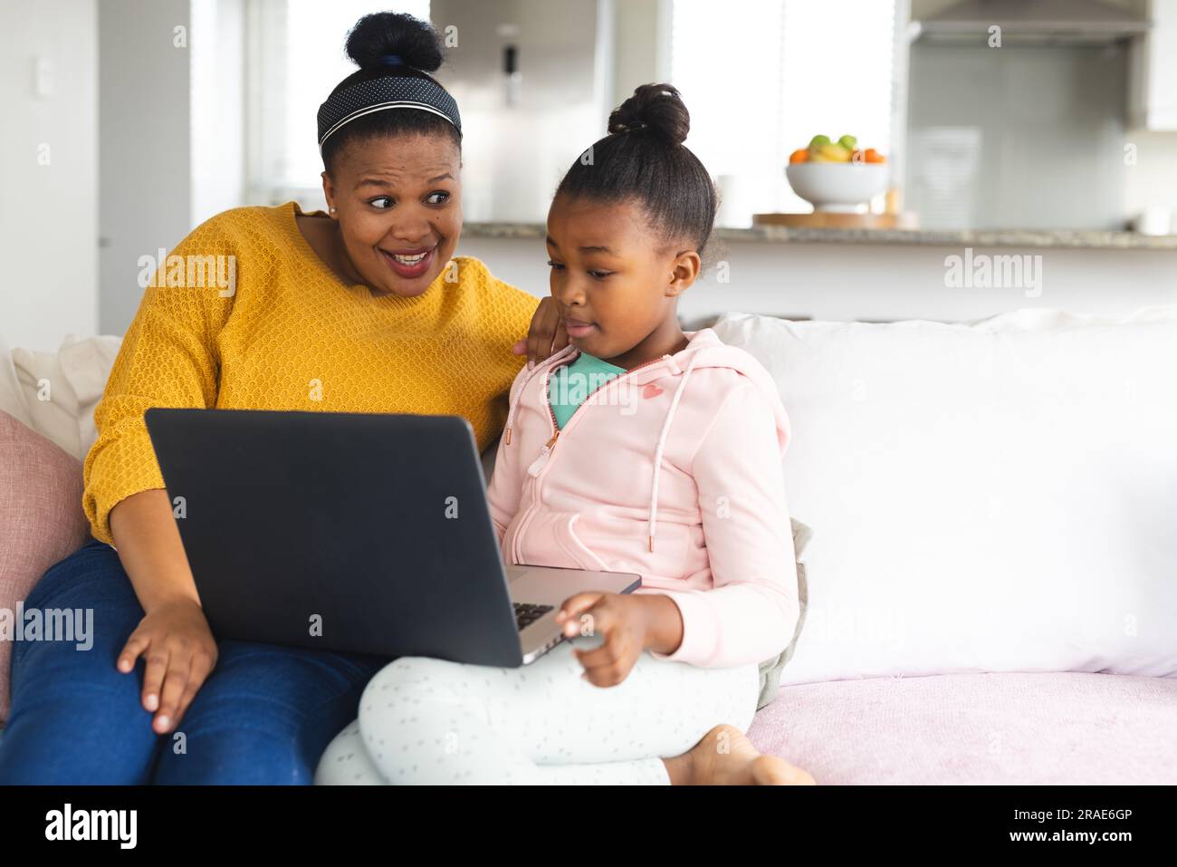 Glückliche afroamerikanische Mutter und Tochter, die auf dem Sofa sitzen und zu Hause ihren Laptop benutzen Stockfoto