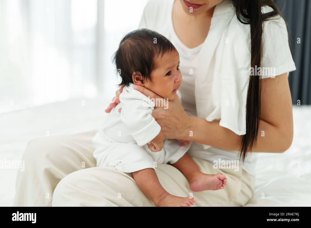 Mutter, die ein Neugeborenes hält und nach der Milchfütterung im Schlafzimmer aufstößt Stockfoto