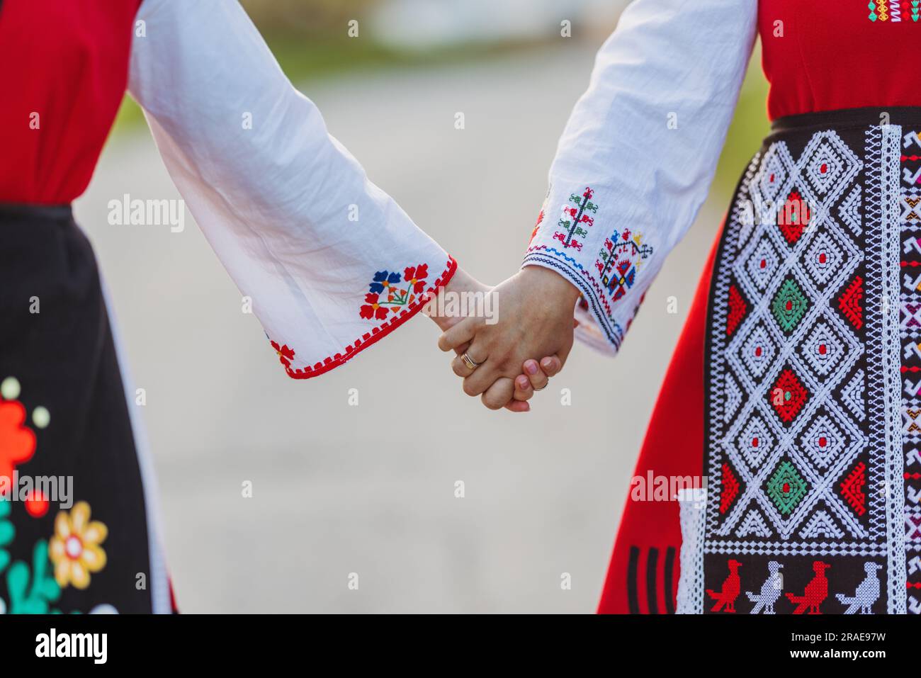 Mädchen in traditionellen bulgarischen ethnischen Kostümen mit folkloristischer Stickerei, die Händchen hält. Der Geist Bulgariens - Kultur, Geschichte und Traditionen. Stockfoto