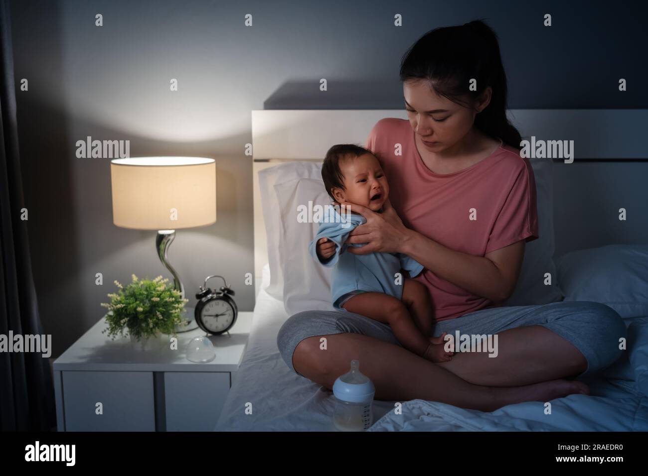 Mutter, die das Baby nach der Milchfütterung auf einem Bett nachts hält und weint Stockfoto
