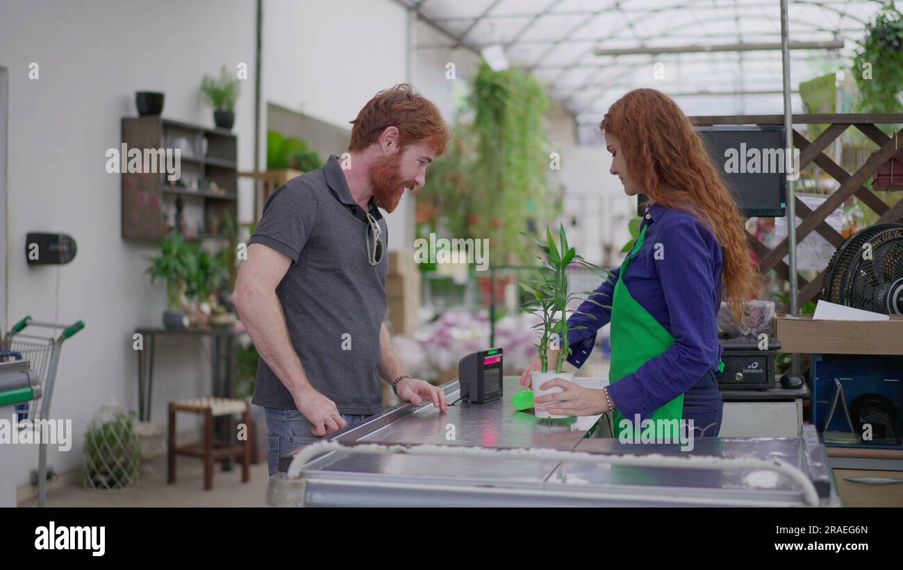 Young man Einkaufsanlage und Telefon für Tap-to-Pay im Flower Shop. Nahtlose kontaktlose Zahlung im Gartenbaugeschäft Stockfoto