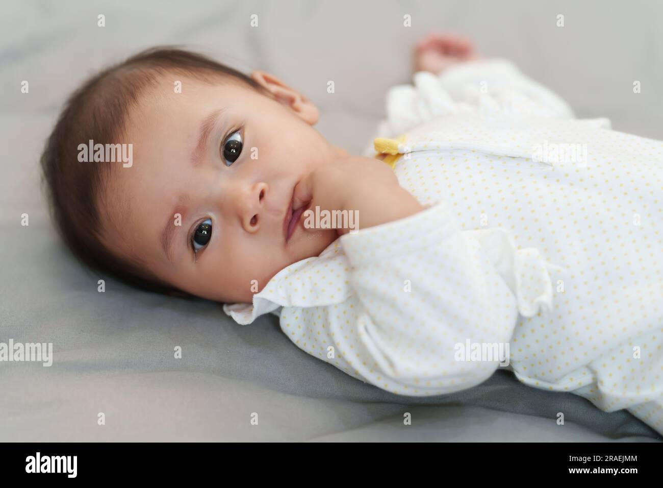 Baby, das die Hände in den Mund steckt und Finger an einem Bett lutscht Stockfoto