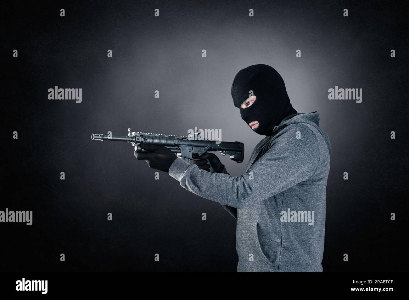 Ein Krimineller trägt schwarze Balaclava und Kapuze mit Sturmgewehr auf dunklem, nebligen Hintergrund Stockfoto