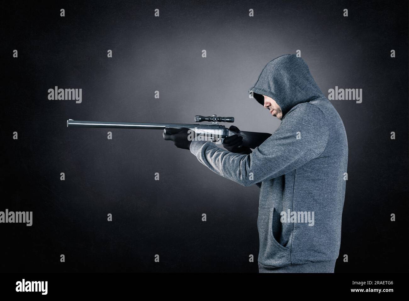 Ein Mann mit Kapuze und Gewehr auf dunklem nebligen Hintergrund Stockfoto