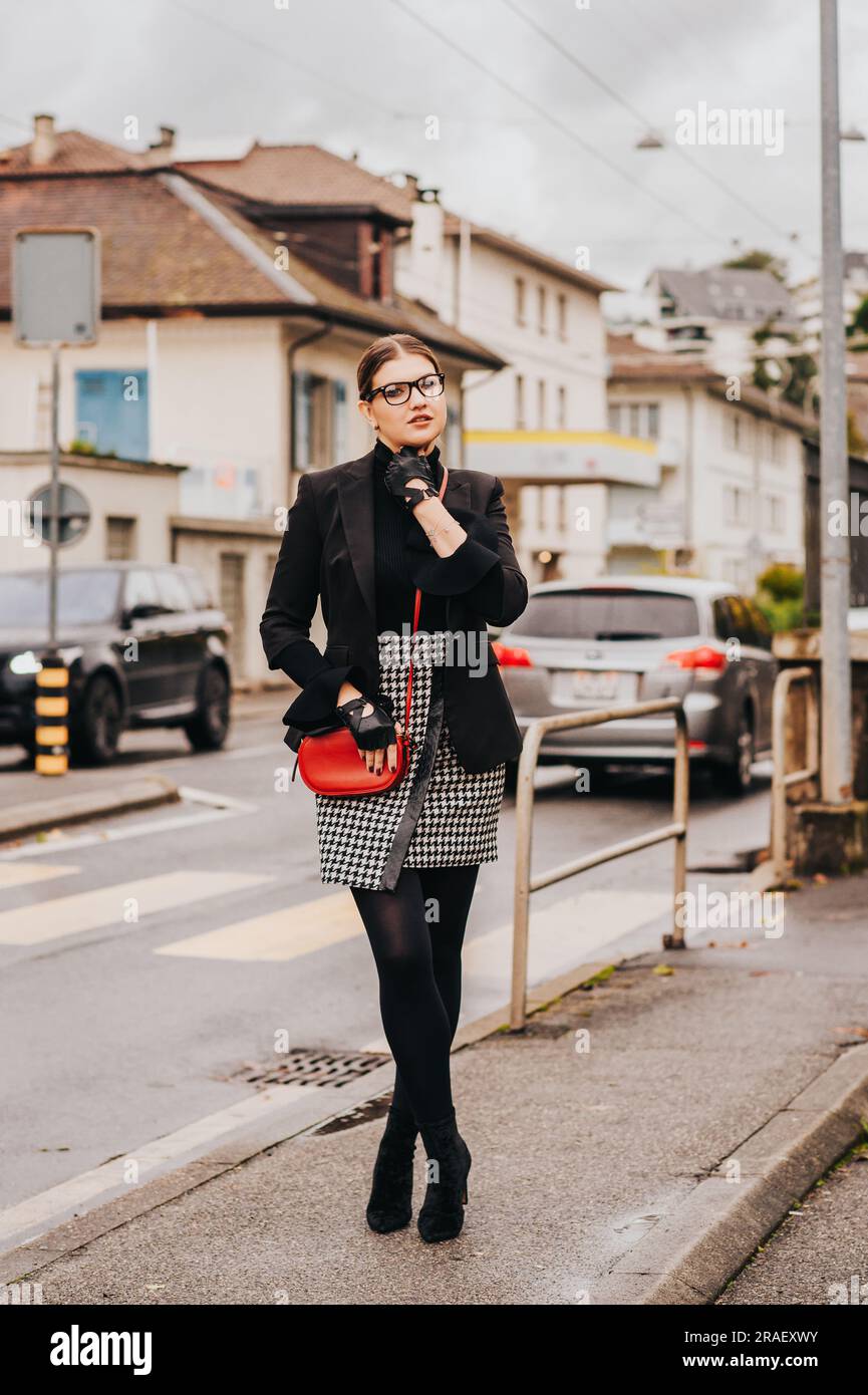 Outdoor-Modeporträt einer jungen, stilvollen Frau, die auf der Straße posiert, eine schwarze Jacke trägt und einen Karo-Rock trägt Stockfoto