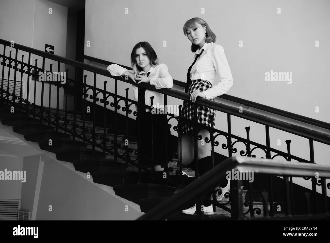 Ein Schwarzweißfoto zeigt zwei Schulmädchen in Uniform, die auf einer Treppe stehen. Das eine ist ein europäisches Mädchen und das andere ein asiatisches Mädchen. Ihre Erfahrung Stockfoto