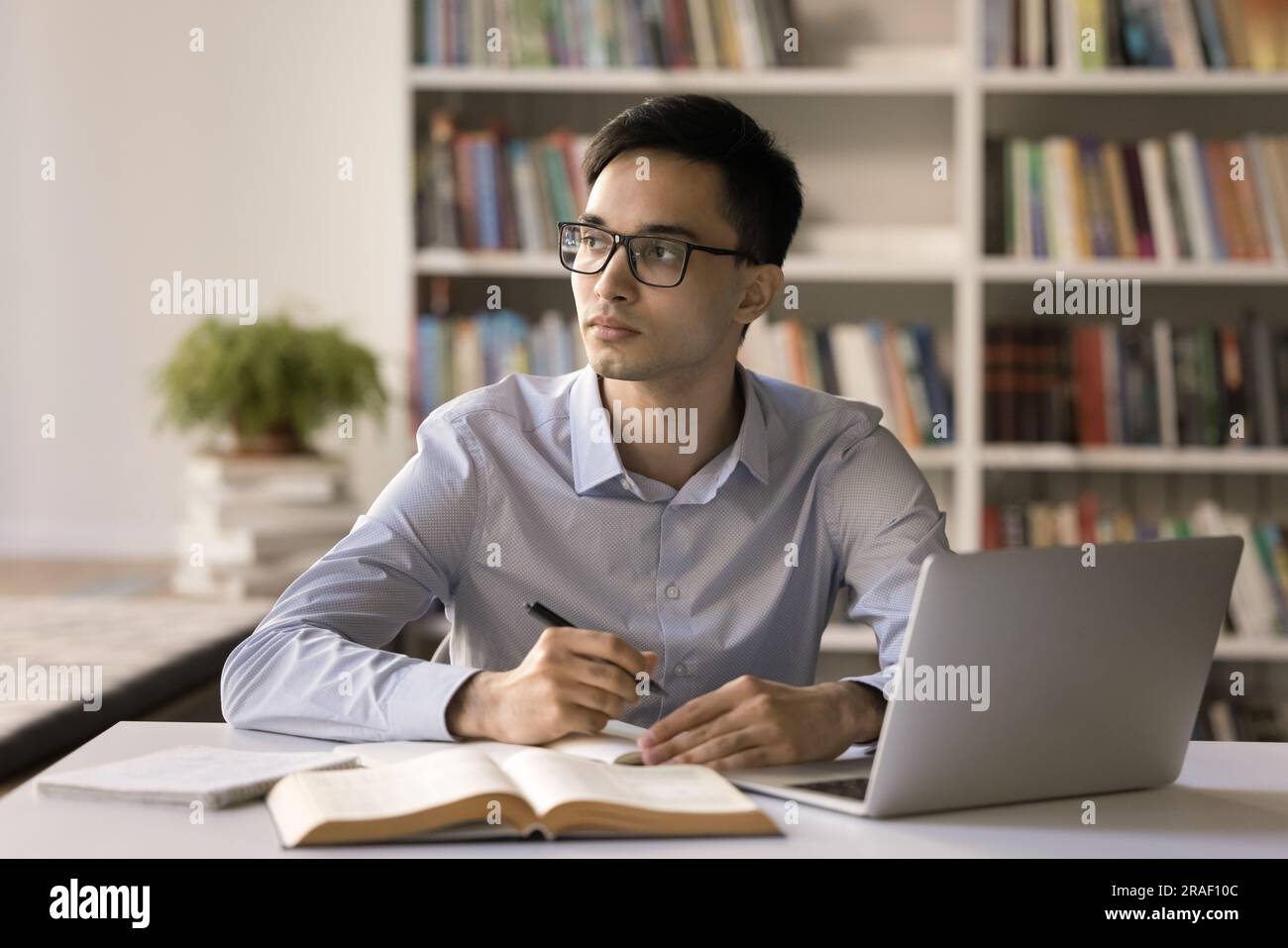 Ein kluger Schüler mit Brille, der in der Universitätsbibliothek lernt Stockfoto