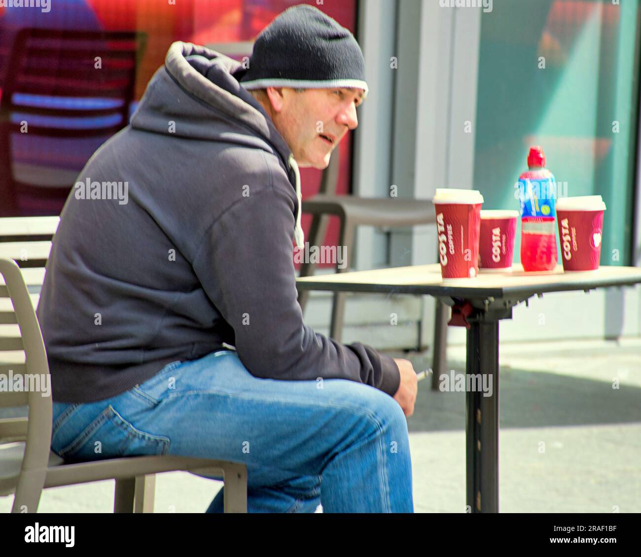 Mann sitzt draußen an einem Tisch in costa mit costa Tassen Stockfoto