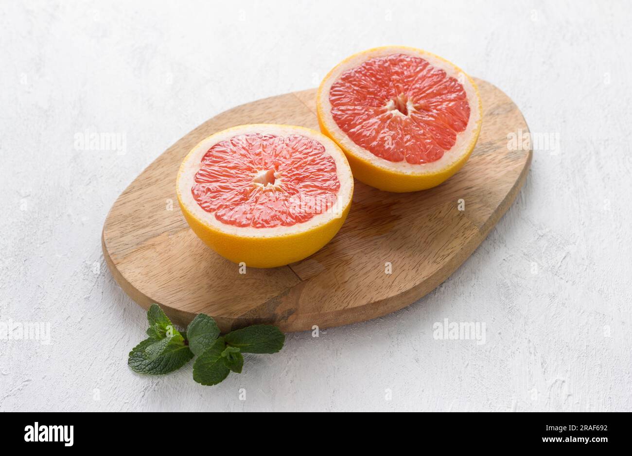 Holzbrett mit zwei Hälften einer Grapefruit auf hellgrauem Hintergrund, Draufsicht. Stockfoto