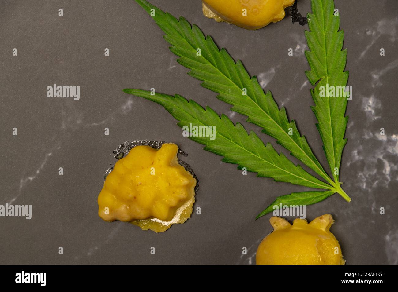 Ein kleines Stück Marihuana-Butter am heißen Tag auf einem schwarzen Marmortisch mit grünem frischem Blatt Stockfoto