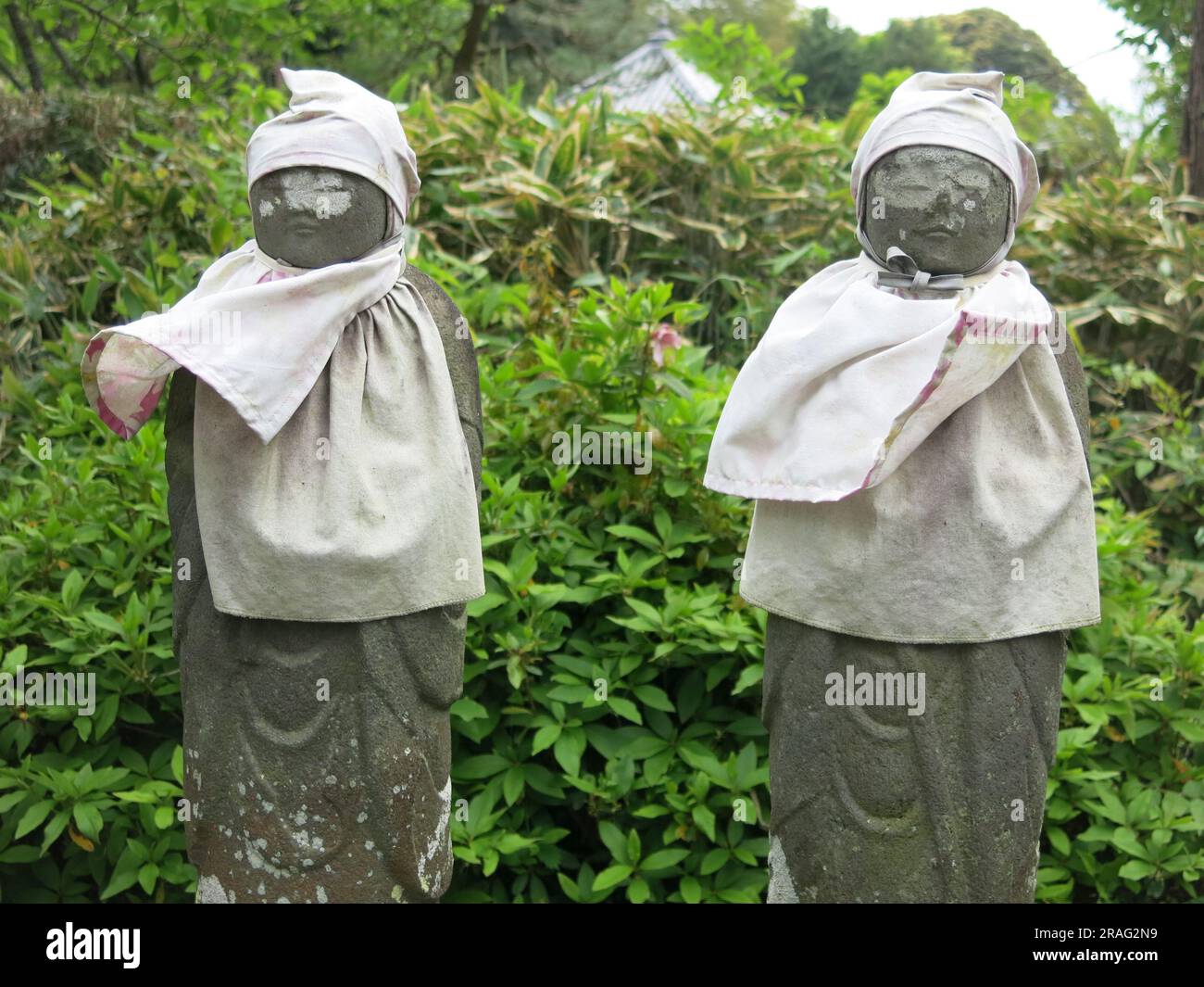 Nahaufnahme von zwei Steinfiguren, Jizo-Statuen, die weiße Mützen und Lätzchen tragen, Kinderwächter im buddhistischen Zen-Tempel von Tokoji in der Nähe von Hagi, Japan. Stockfoto