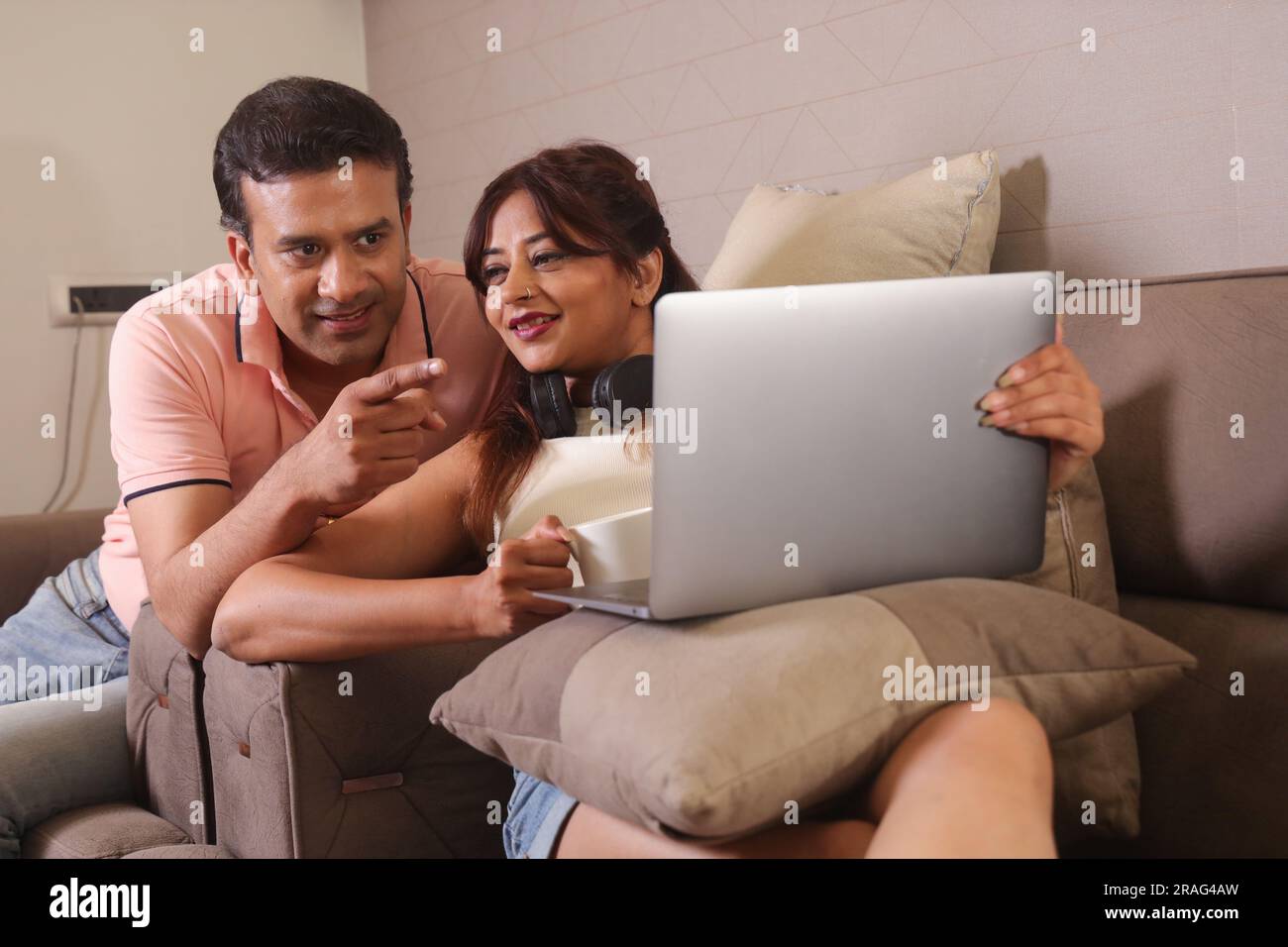 Indisches glückliches Paar, das auf dem Sofa sitzt und mit einem Laptop online surft. Und eine Tasse Kaffee trinken und glückliche Momente. Stockfoto