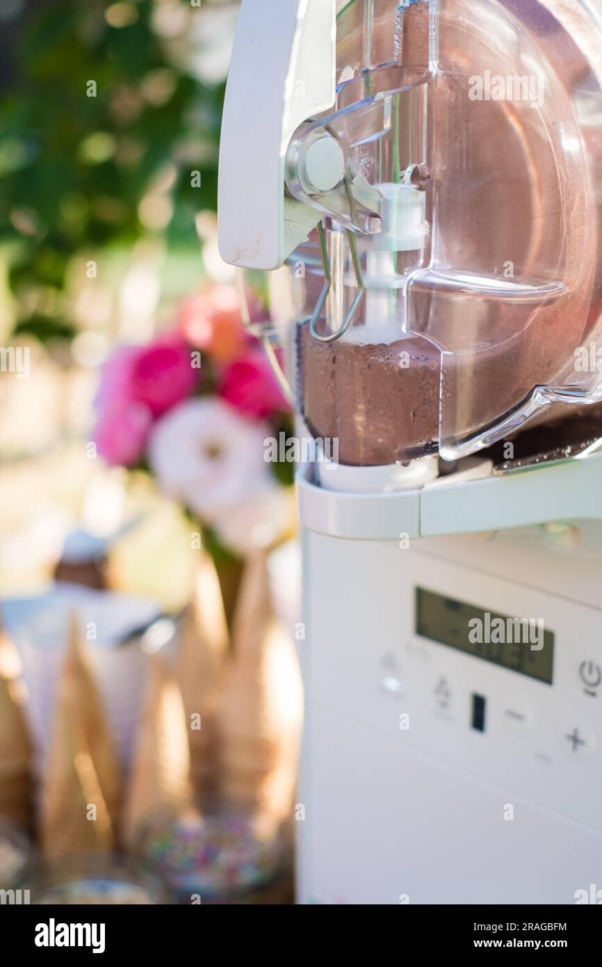 Eiscreme-Maschine mit Waffelmuscheln, Tassen und Streuseln bei der Sommerparty im Garten. Stockfoto