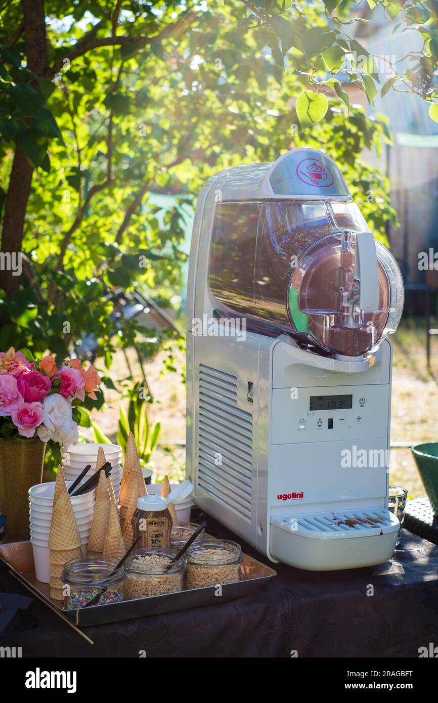 Tallinn, Estland - 30. Juni 2023: Weicheismaschine Ugolini mit Waffelkonusbechern und Streuseln bei einer Sommerparty im Garten. Stockfoto