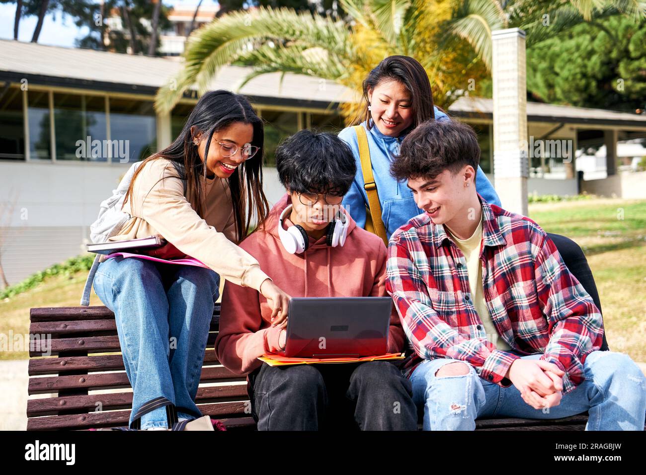 Eine Gruppe von vier Schülern, die mit einem Notebook im Freien lächeln und Spaß haben. Teenager Generation z Stockfoto