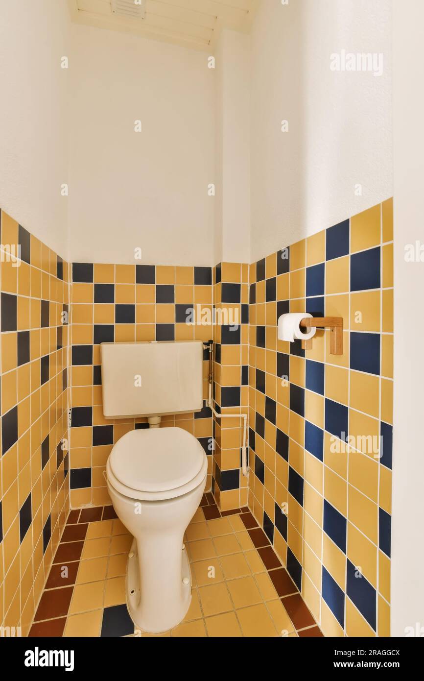 Ein Badezimmer mit gelben und blauen Fliesen an den Wänden, weiße Toilettenschüssel in der Ecke neben dem Waschbecken Stockfoto