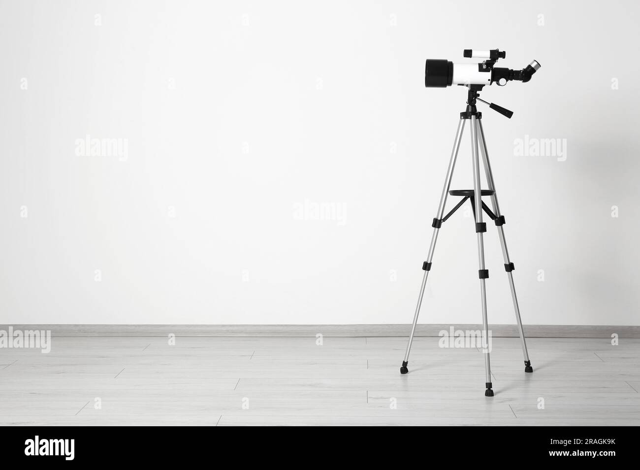 Stativ mit modernem Teleskop nahe der weißen Wand. Platz für Text Stockfoto