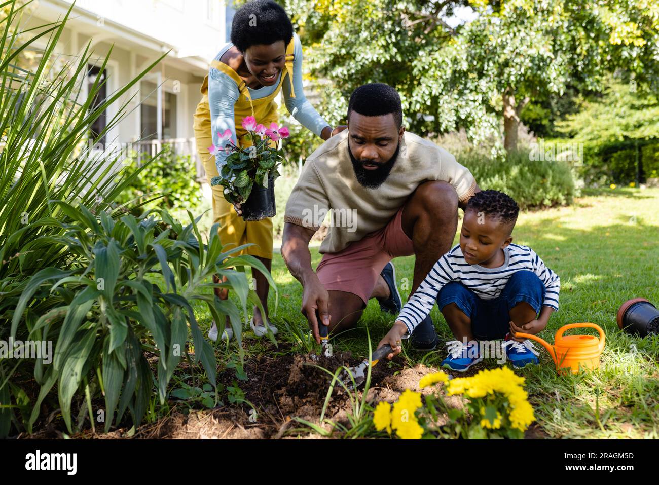 Eine afroamerikanische Frau, die Blumen hält, während Vater und Sohn Dreck auf Grünland im Hof graben Stockfoto