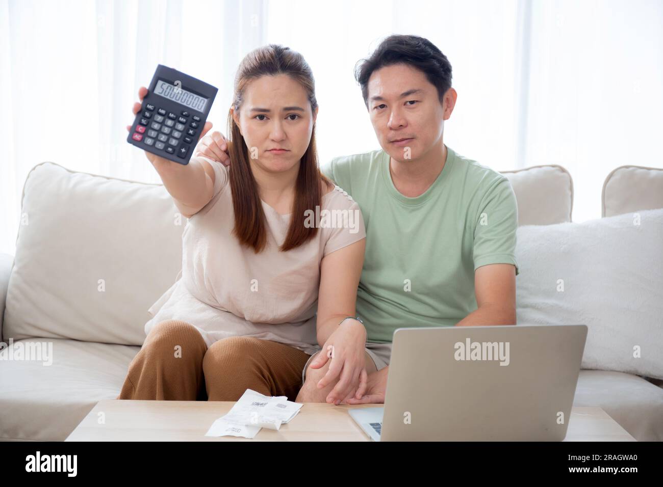 Unglückliches junges asiatisches Paar, das auf dem Sofa sitzt, zeigt einen Taschenrechner mit Kredit und Spesen im Wohnzimmer zu Hause, Mann und Frau planen über Finanzen und Mo Stockfoto