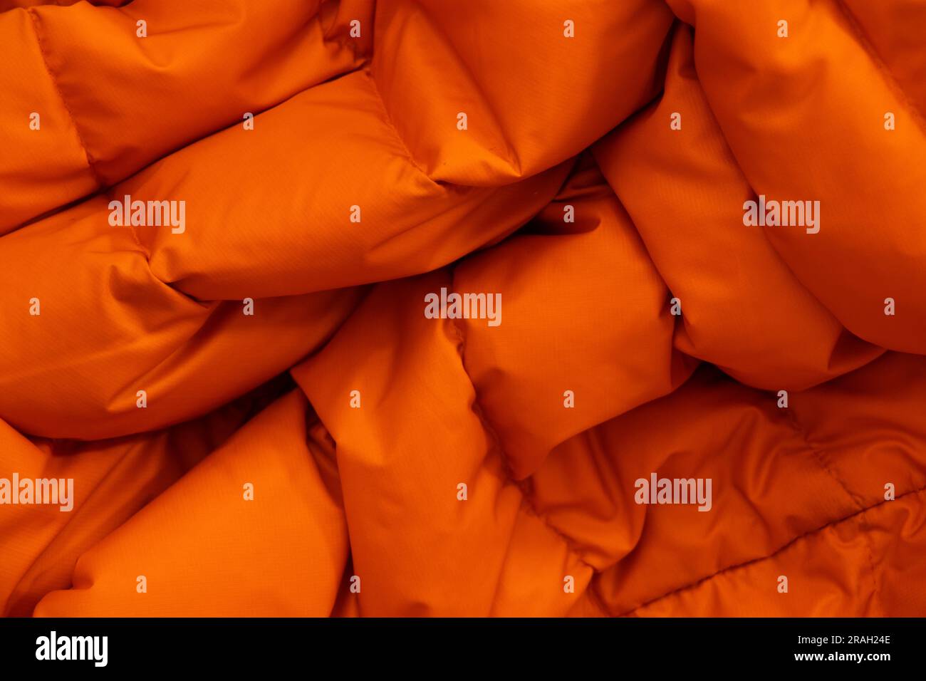 Orangefarbenes Gewebe einer warmen Puffjacke als Hintergrund aus nächster Nähe Stockfoto