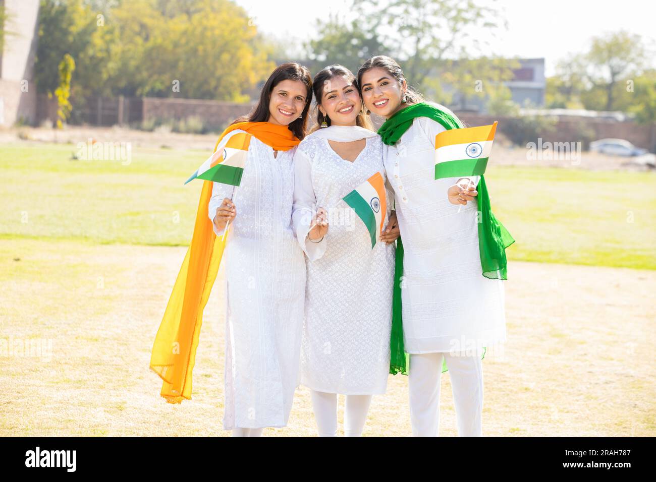Drei junge, wunderschöne Frauen in traditionellem weißen Kleid mit indischer Flagge. Sie stehen zusammen im Park und feiern den Unabhängigkeitstag Stockfoto