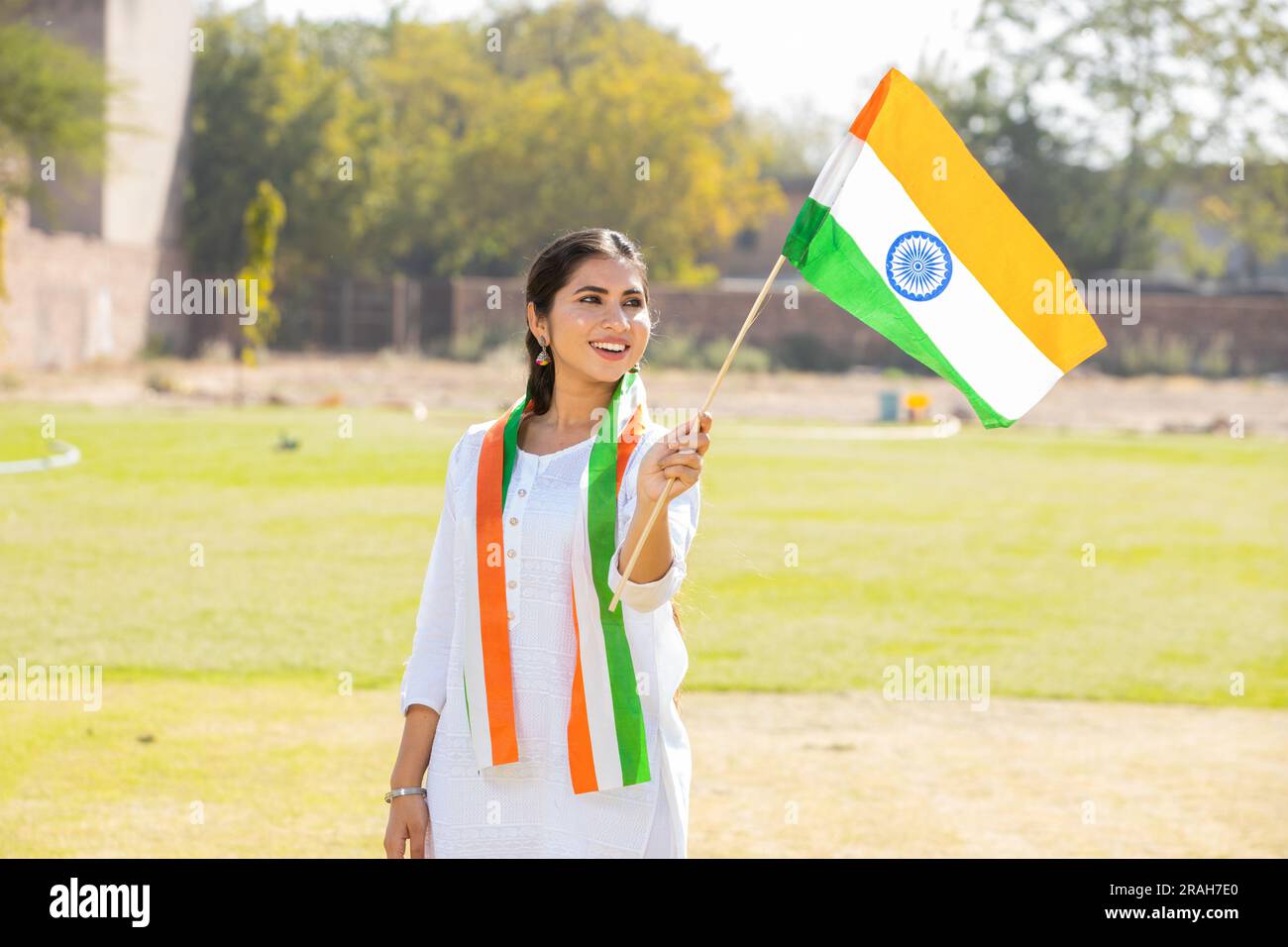 Junge, schöne Frau in traditionellem weißen Kleid mit indischer Flagge und Webfahne, während sie im Park steht und den Unabhängigkeitstag oder die Republik feiert Stockfoto