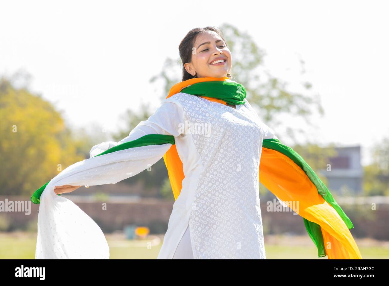 Porträt einer glücklichen jungen indischen Frau, die traditionelle weiße Kurta und dreifarbige Duppata trägt, die im Park laufen. Wir feiern den Unabhängigkeitstag oder die Republik da Stockfoto