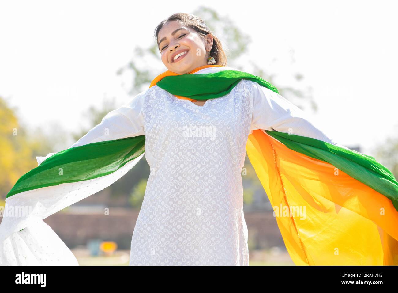 Porträt einer glücklichen jungen indischen Frau, die traditionelle weiße Kurta und dreifarbige Duppata trägt, die im Park laufen. Wir feiern den Unabhängigkeitstag oder die Republik da Stockfoto
