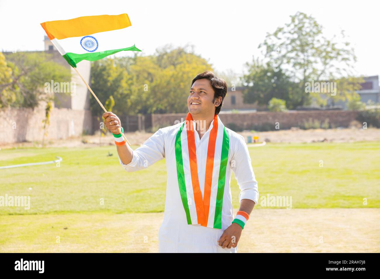 Glücklicher junger Mann in traditionellem weißen Kleid mit indischer Flagge und Webflagge, während er im Park steht und den Unabhängigkeitstag oder den Republikstag feiert. Stockfoto