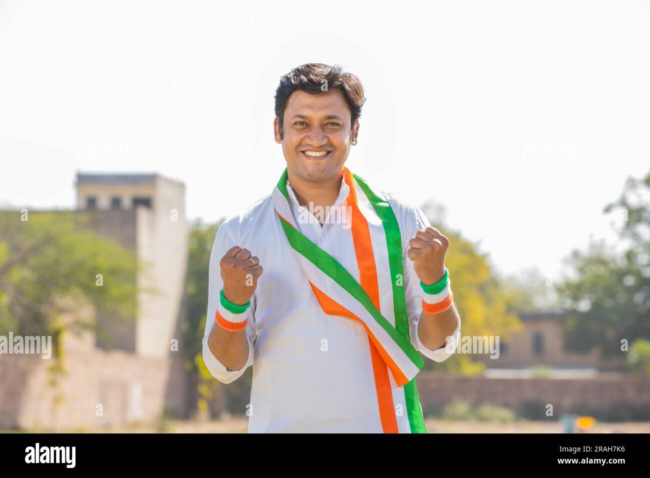 Porträt eines fröhlichen, gutaussehenden jungen Mannes mit traditioneller weißer Kurta und dreifarbigen Duppata im Park. Fans jubeln für das indische Team-Fest Stockfoto