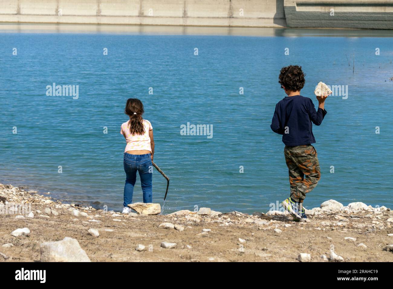 Zwei Kinder werfen Steine in das Wasser eines Dammes Stockfoto
