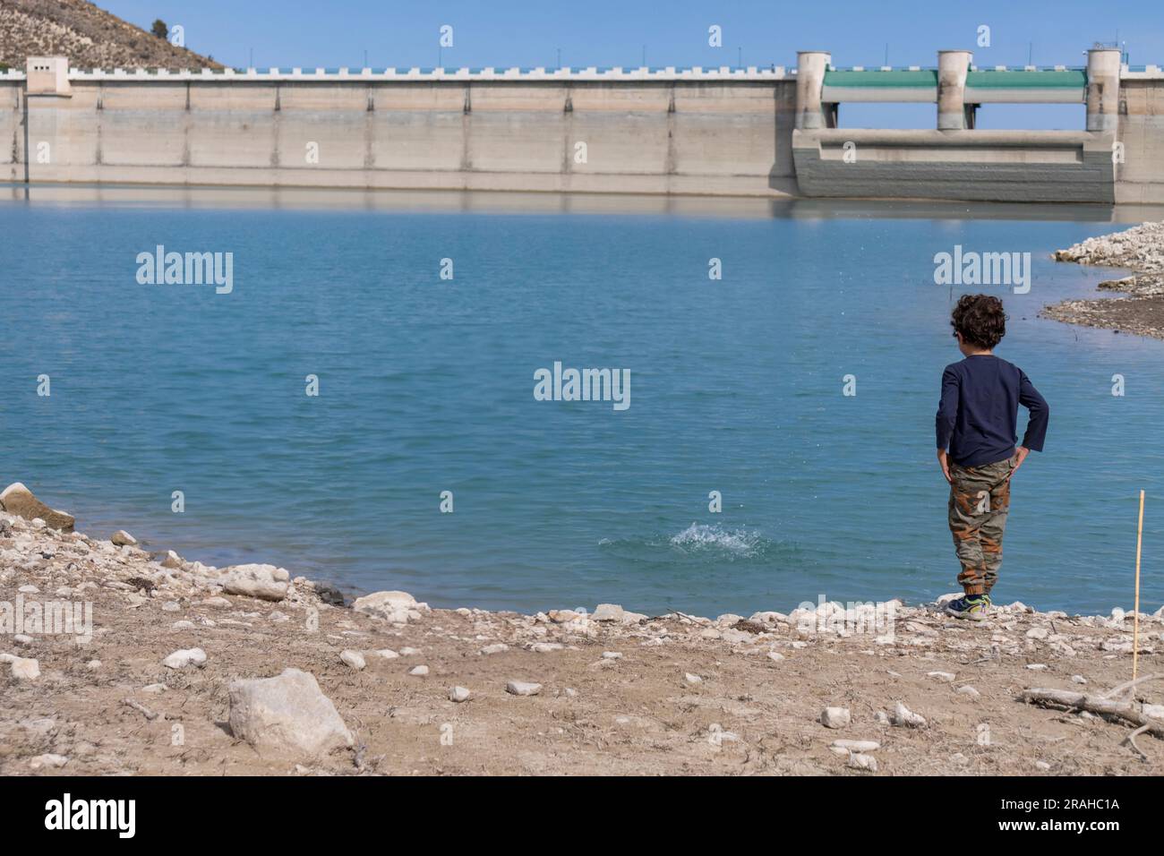 Ein Junge, der Steine an einem Damm ins Wasser wirft Stockfoto