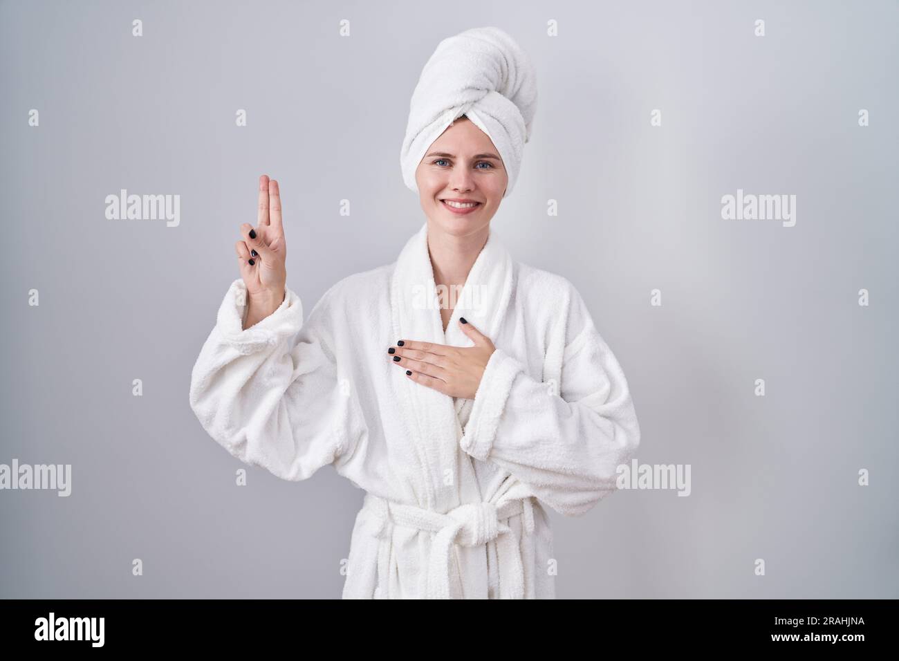 Blonde weiße Frau, die im Bademantel lächelt, mit der Hand auf der ...